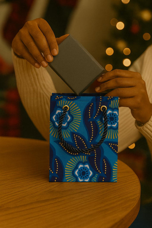 Person opening a blue, dark blue, white & gold gift bag with decorative patterns on a wooden surface.