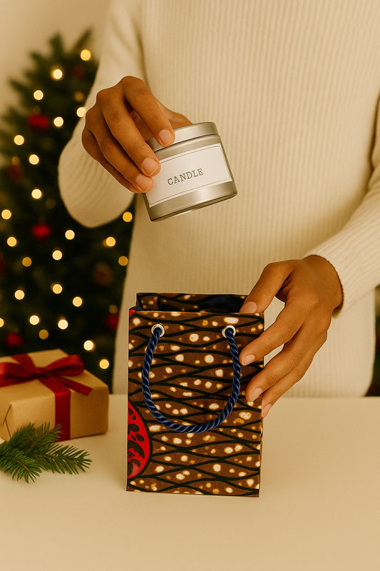 Person placing a candle in a dark blue, dark brown, cream, & maroon gift bag with Christmas decorations in the background