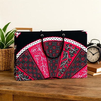Decorative black, fuchsia, and white patterned bag on a wooden surface with a plant and clock in the background.