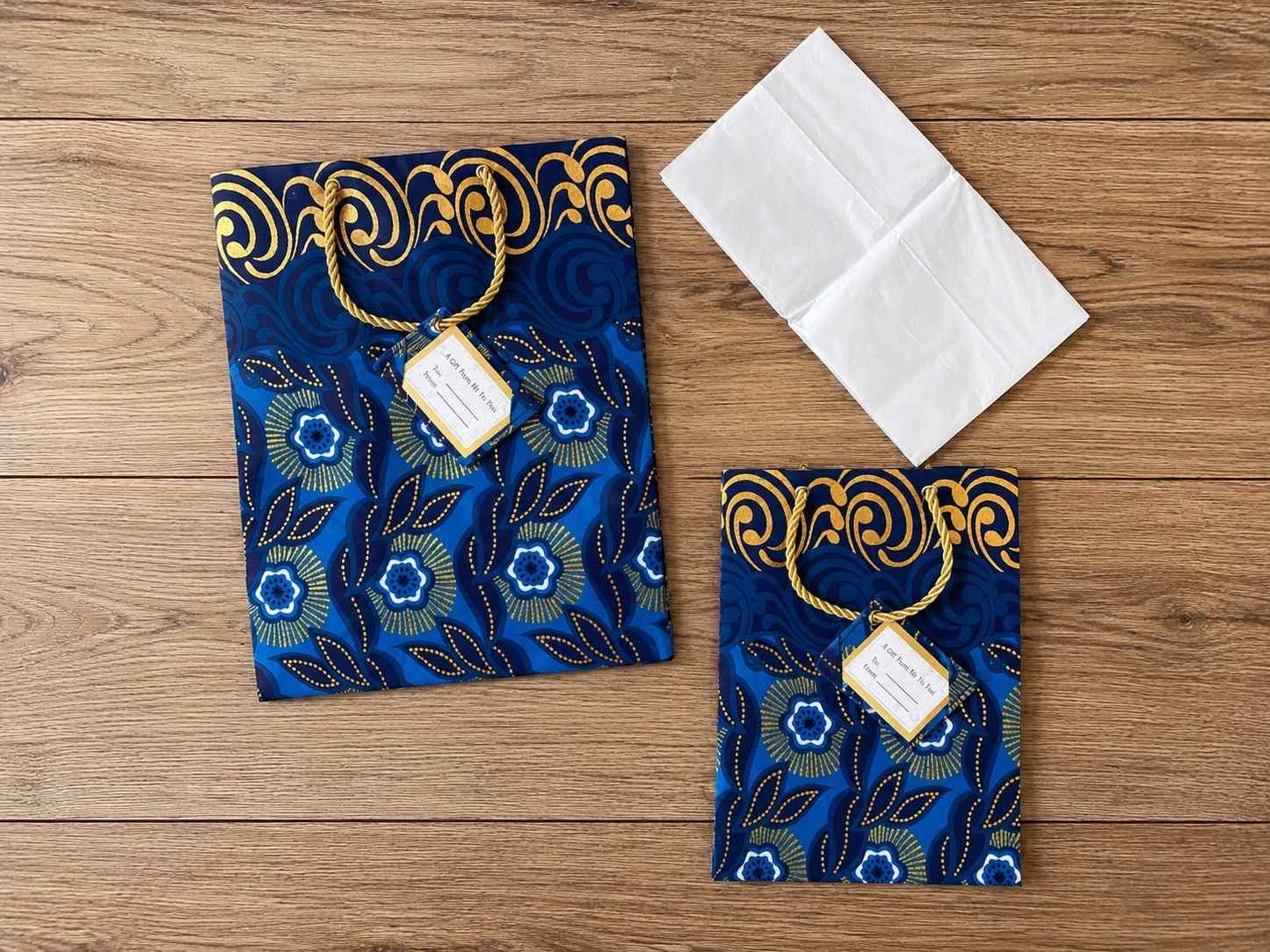 Two blue decorative gift bags gold patterns, gift tags and tissue paper on a wooden surface