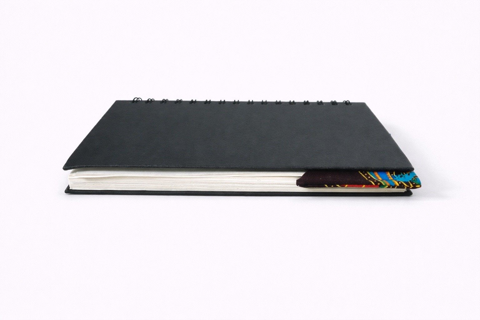 Black spiral-bound notebook with a dark brown, blue, red, & yellow corner bookmark on a light gray background