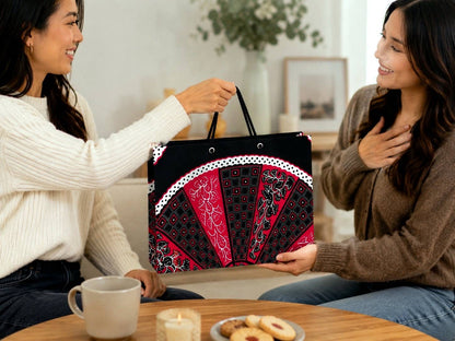 Two women sitting at a table with a decorative black, fuchsia, and white bag between them, in a cozy indoor setting.