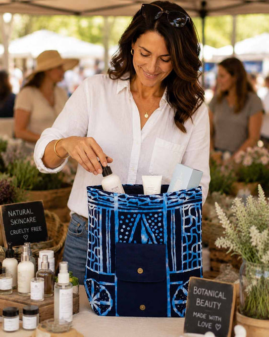 Woman at a market stall with natural skincare products and a blue and white patterned bag.