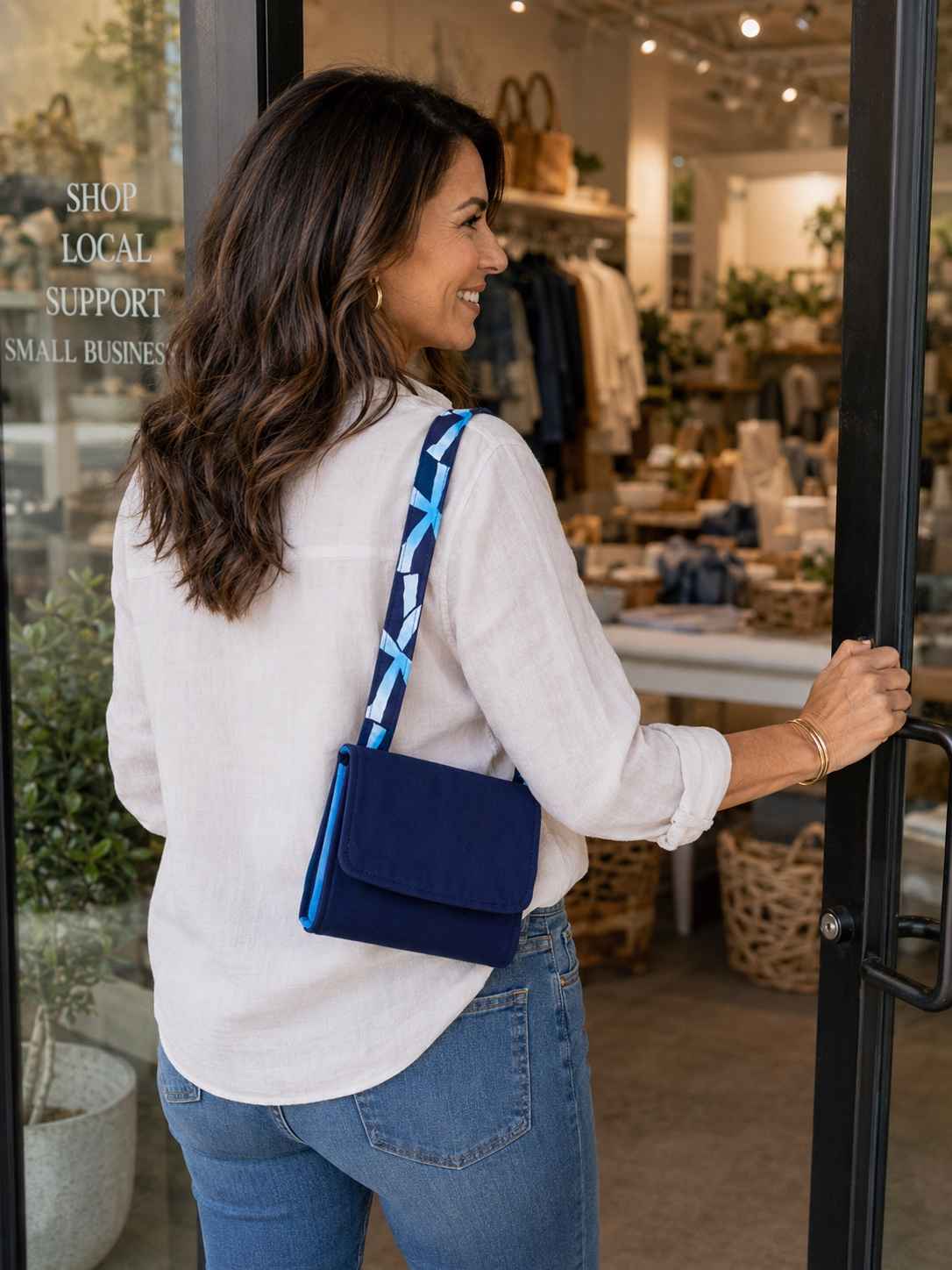 Woman entering a store with a blue and white folded market bag, with 'Shop Local Support Small Businesses' text.