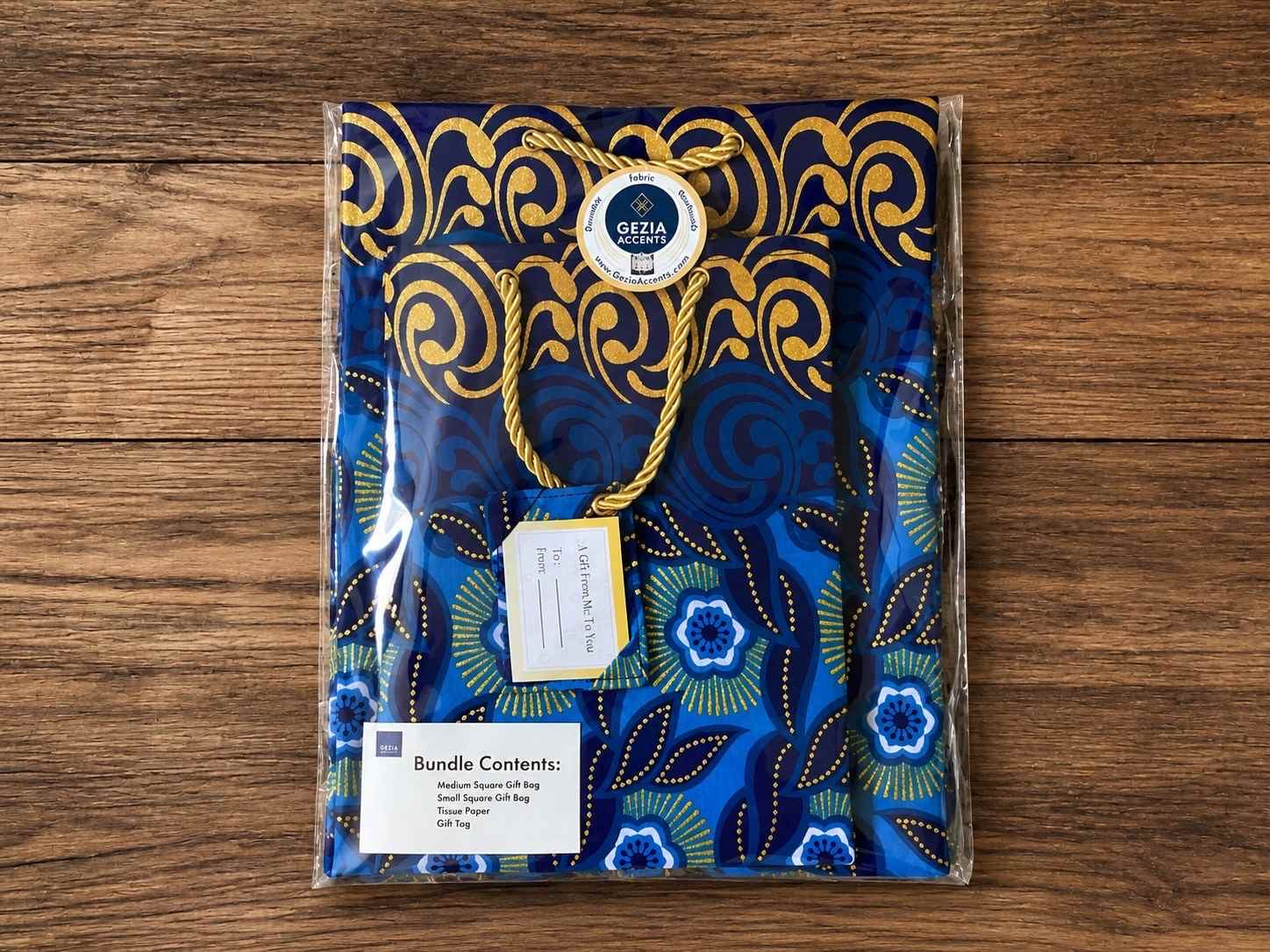 Packaged gift bags with decorative blue and gold pattern, tissue paper, and gift tags on a wooden surface