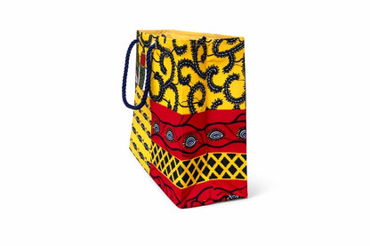 Side view of set of socks, a mug with chocolates, and a colorful red, yellow, white, and dark blue patterned bag on a white background
