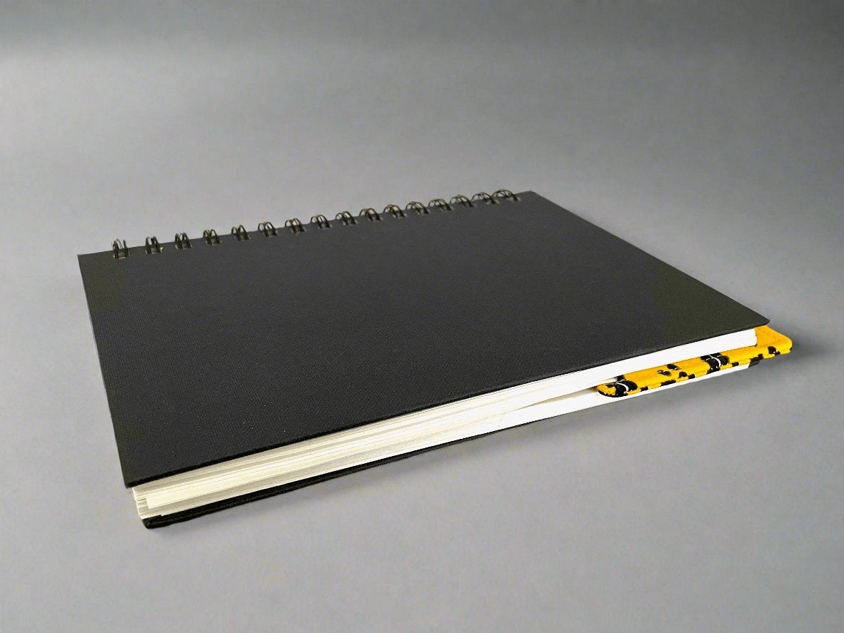 Black notebook with a corner bookmark in yellow accents on a gray background
