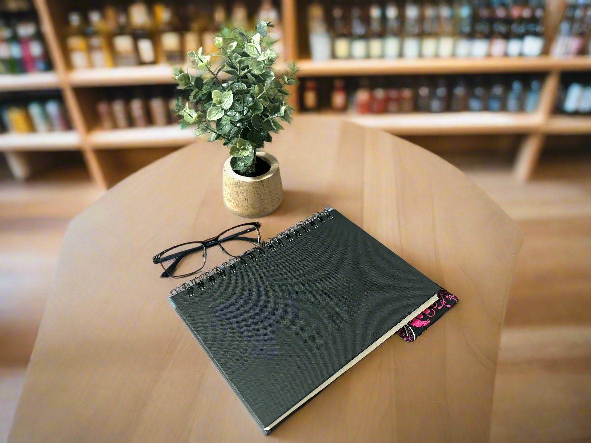 Black notebook with a corner bookmark in pink and white accents on a gray background
