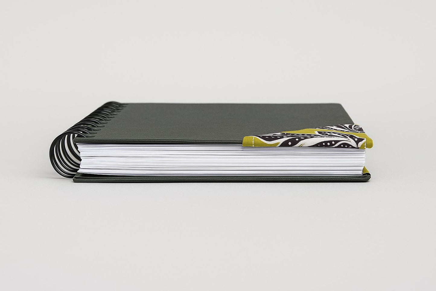 Black notebook with a corner bookmark in green, brown, & white accents on a gray background