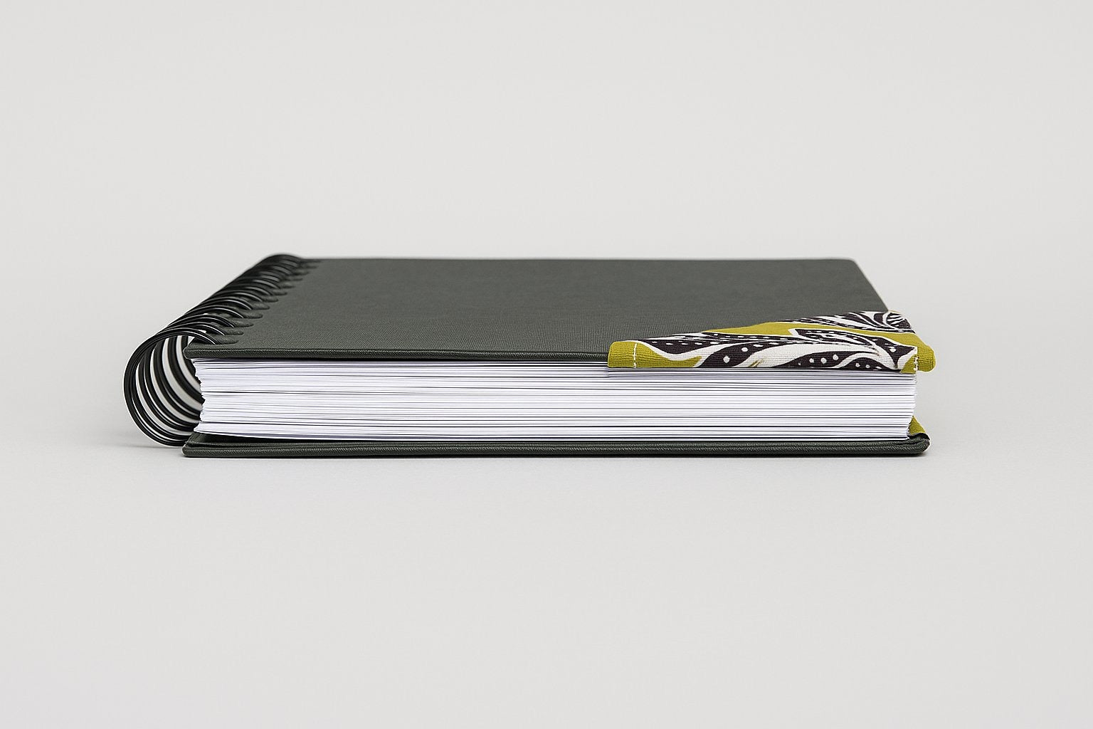 Black notebook with a corner bookmark in green, brown, & white accents on a gray background