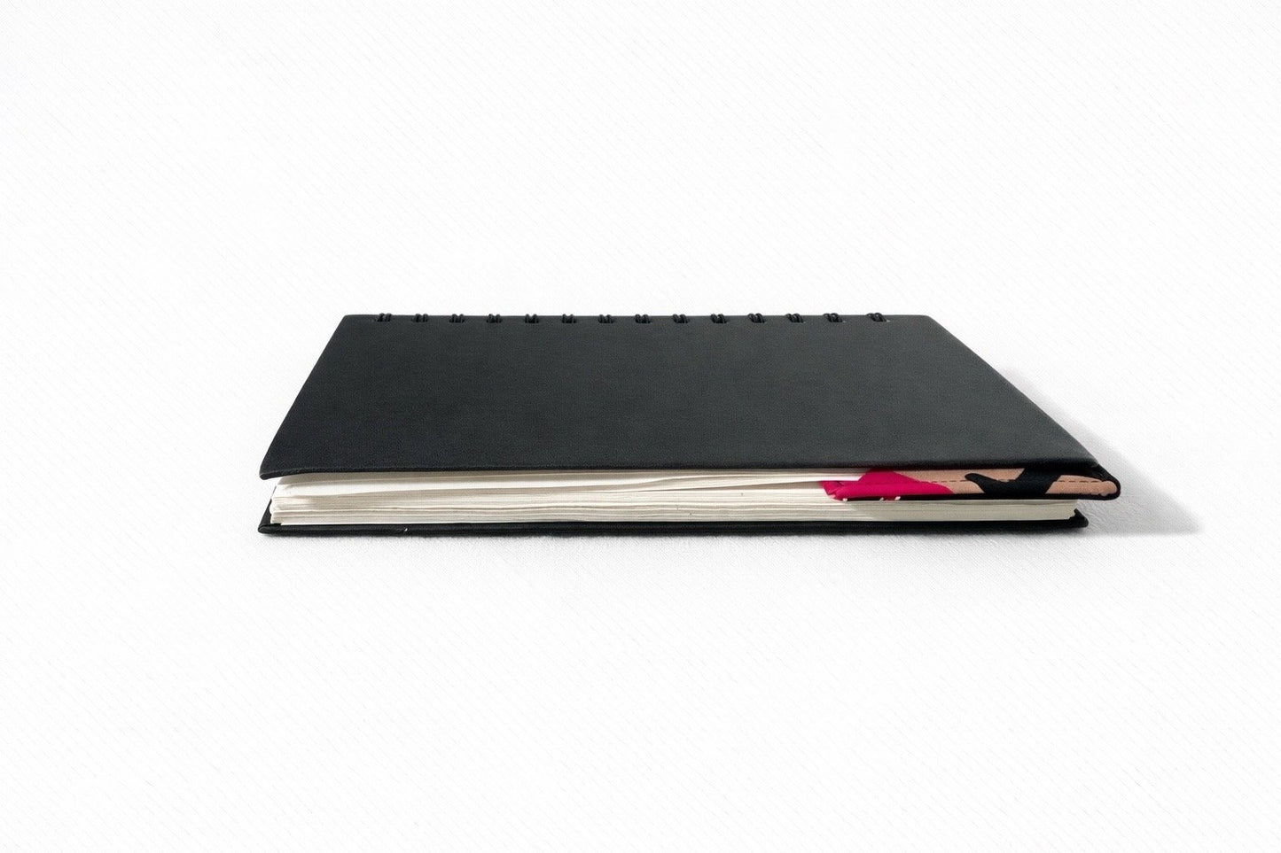 Black notebook with a corner bookmark in black, pink, beige, & cream accents on a gray background