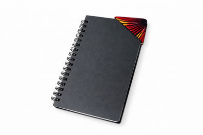 Black notebook with a black corner bookmark with yellow & red accents on a gray background