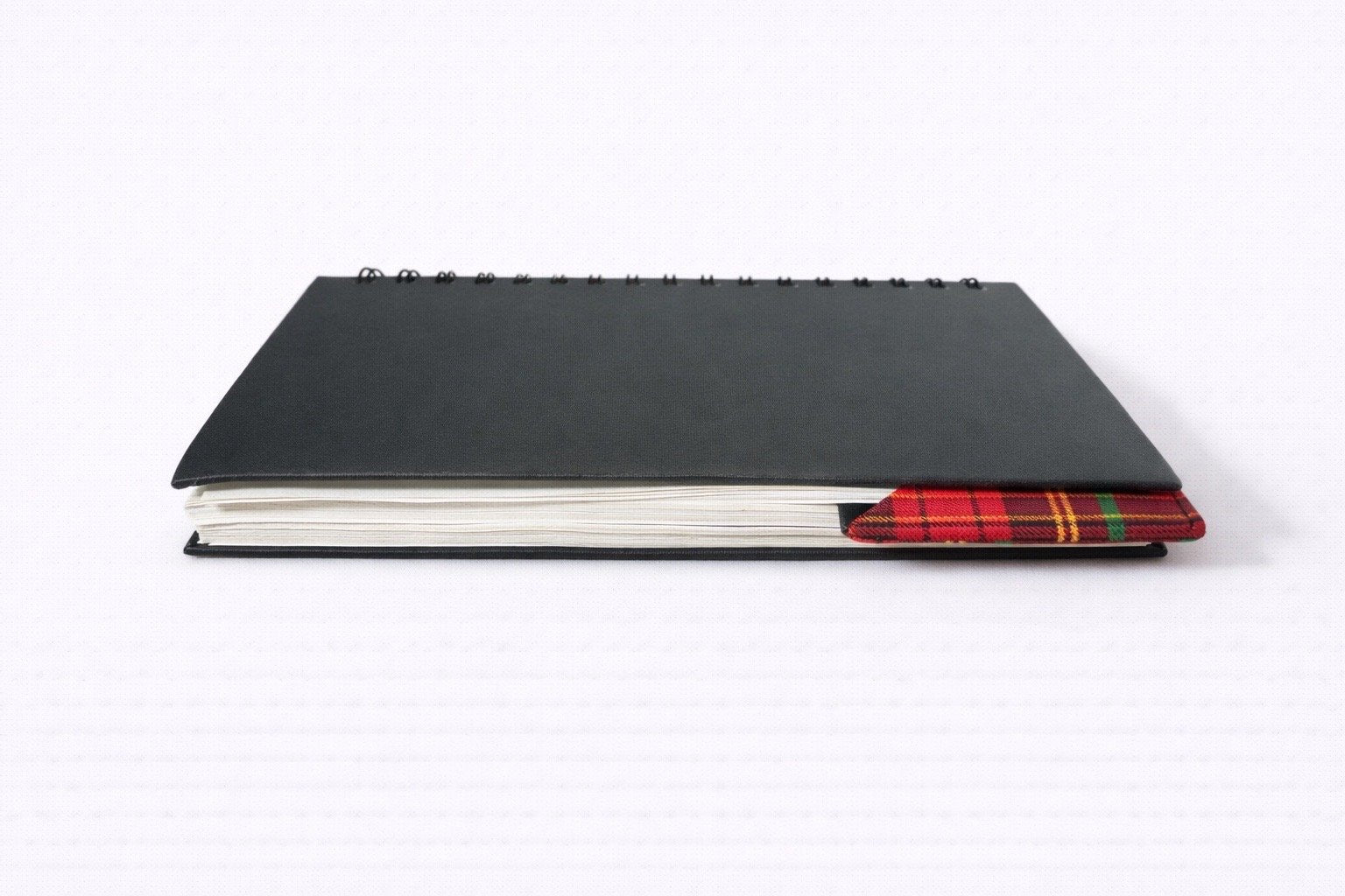 Black notebook with a black corner bookmark in red, green, & gold accents on a gray background