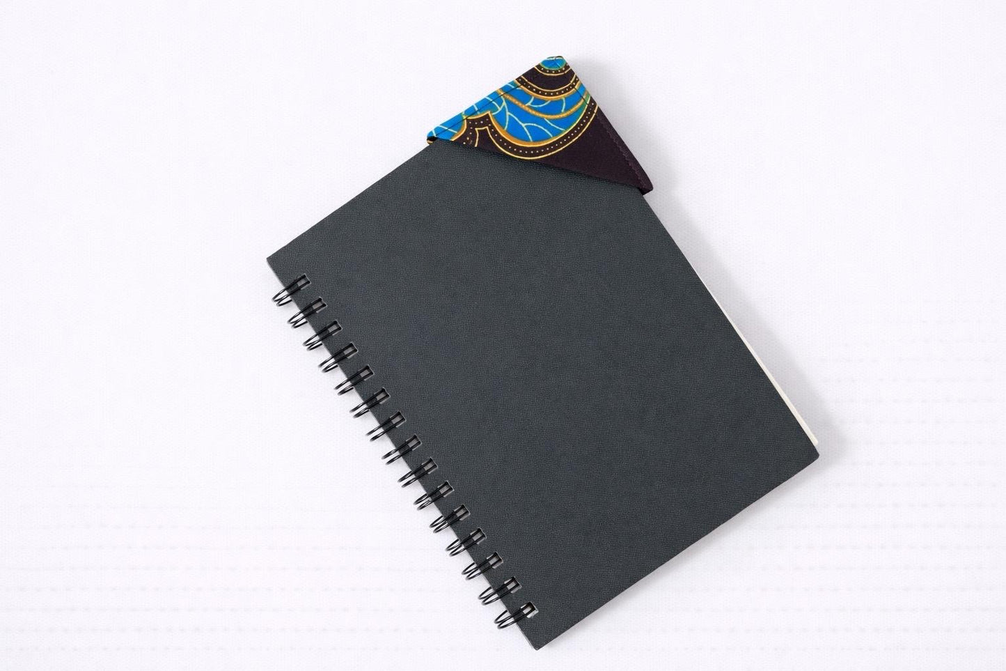 Black notebook with a corner bookmark in dark brown, red, blue, & yellow accents on a gray background