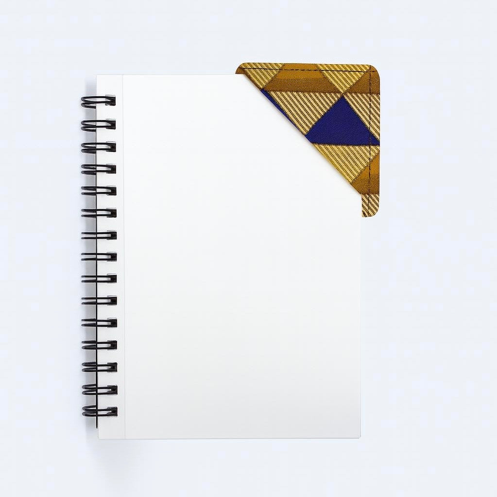 Black notebook with a corner bookmark in gold, brown, & blue accents on a gray background
