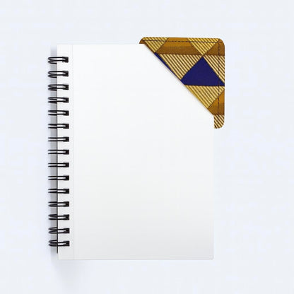 Black notebook with a corner bookmark in gold, brown, & blue accents on a gray background