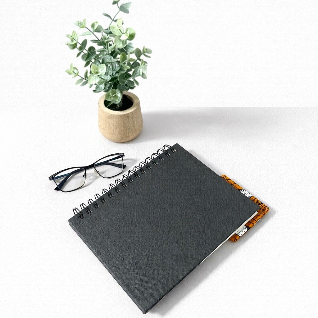 Black notebook with a corner bookmark in orange, black, & white accents on a gray background