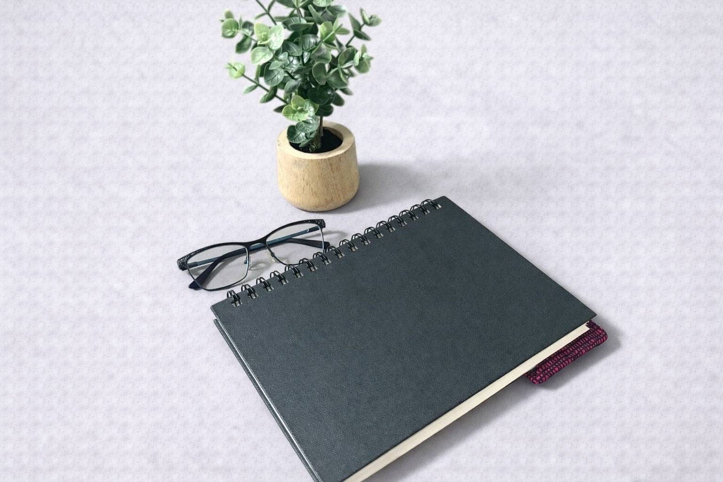 Black notebook with a corner bookmark in pink, brown, cream & gold accents on a gray background
