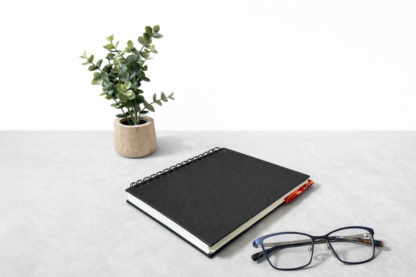 Black notebook with a corner bookmark in red, maroon, pink & gold accents on a gray background