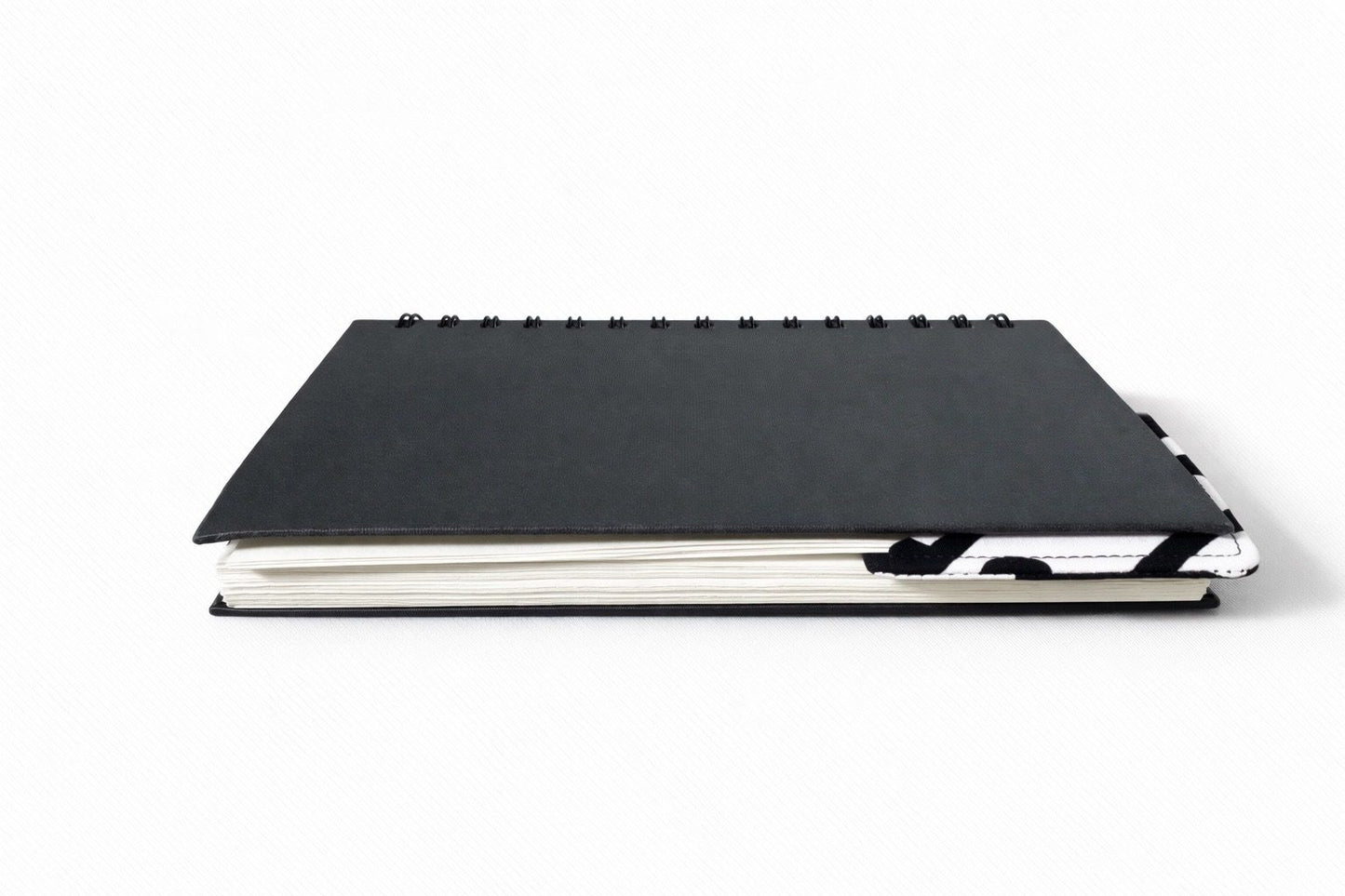 Black notebook with a corner bookmark in white, red & black accents on a gray background