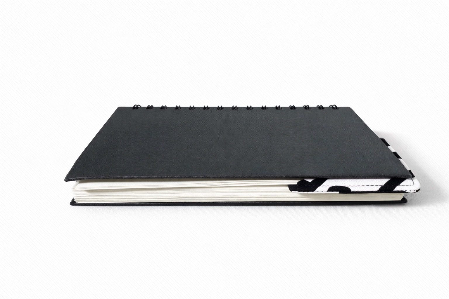 Black notebook with a corner bookmark in white, red & black accents on a gray background
