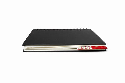 Black notebook with a corner bookmark in white, red, & gold accents on a gray background