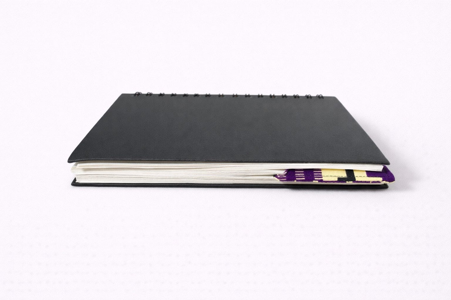 Black notebook with a corner bookmark in yellow, purple, & black accents on a gray background