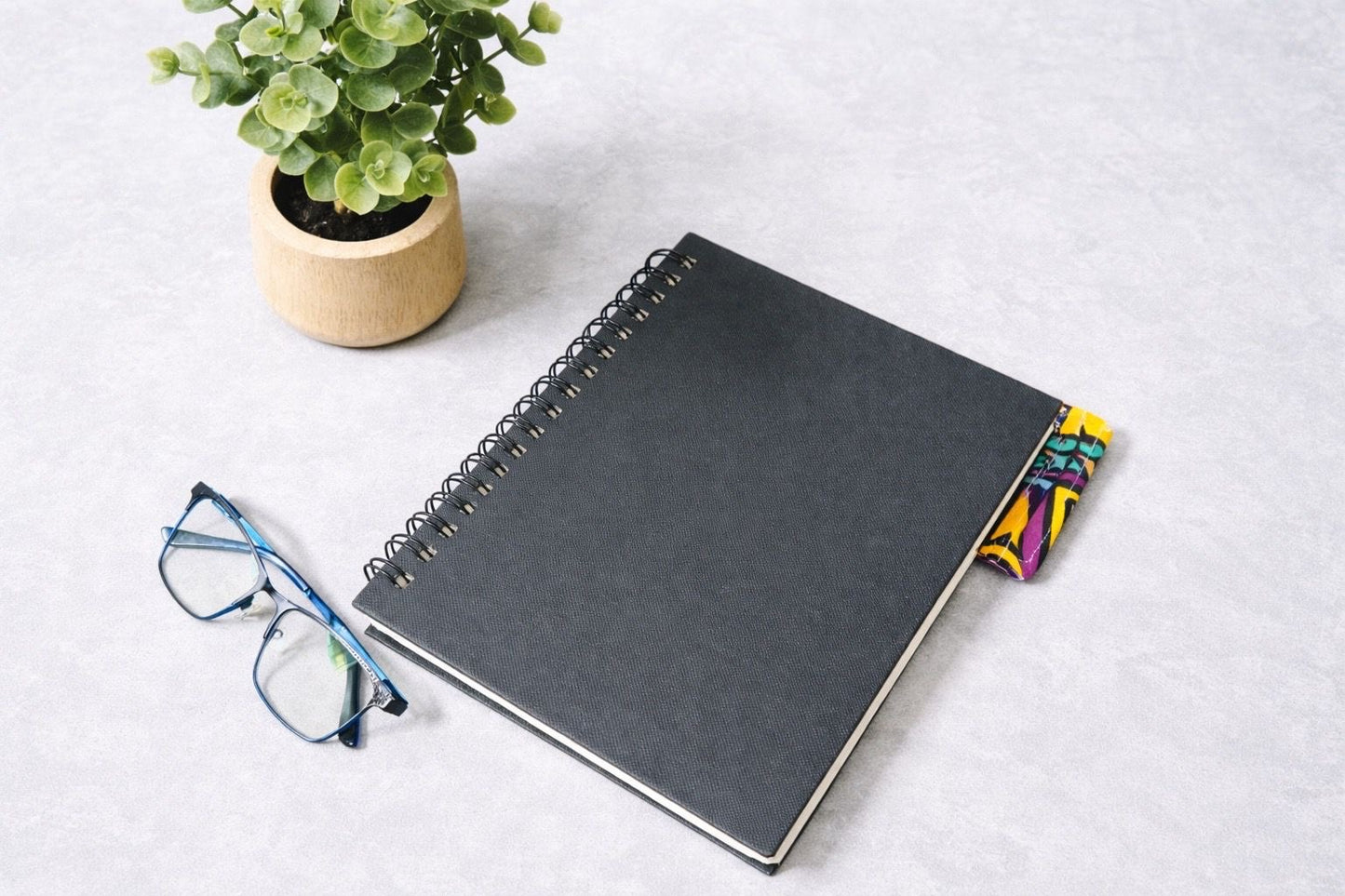Black notebook with a corner bookmark in yellow, purple, green, taupe, & white accents on a gray background