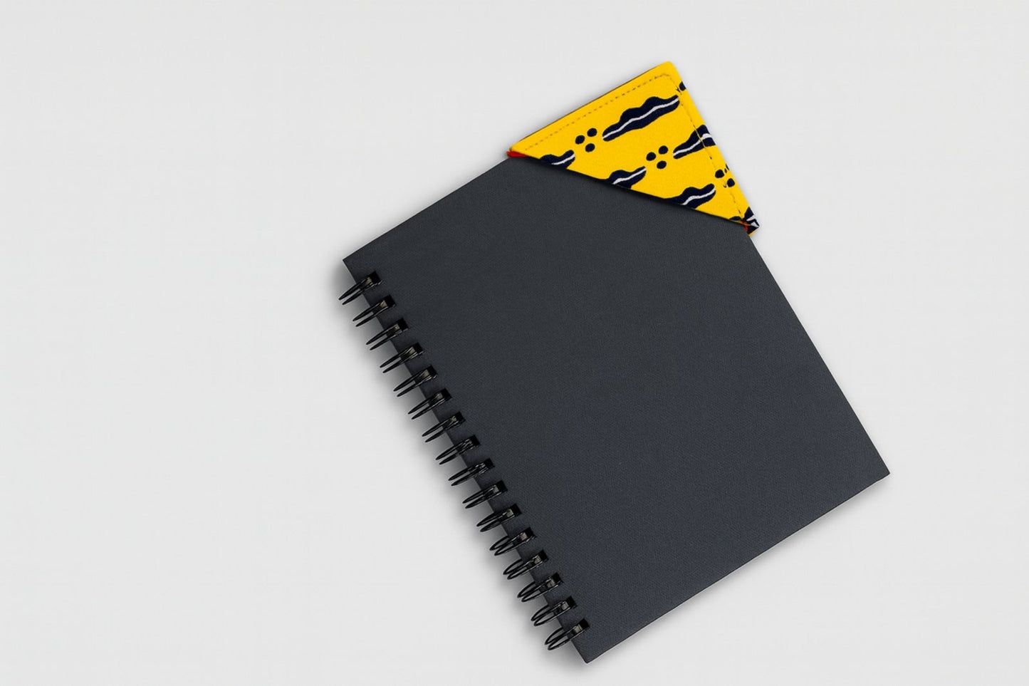 Black spiral-bound notebook with a yellow and blue corner bookmark on a light gray background