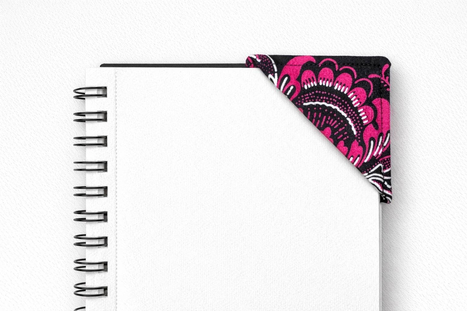 Black spiral-bound notebook with a black, pink & white corner bookmark on a light gray background