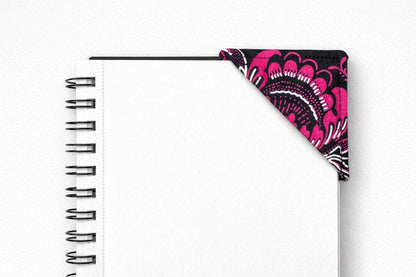 Black spiral-bound notebook with a black, pink & white corner bookmark on a light gray background