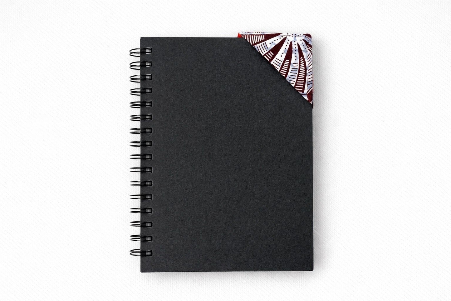 Black spiral-bound notebook with a red, brow, & white corner bookmark on a light gray background