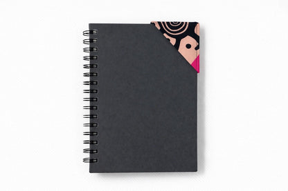 Black spiral-bound notebook with a black, pink, beige, & cream corner bookmark on a light gray background