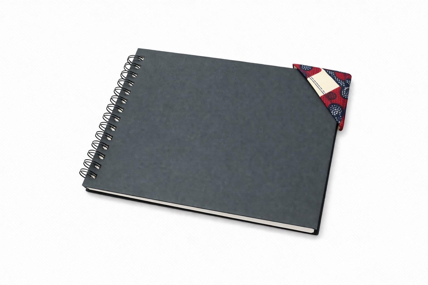 Black spiral-bound notebook with a cream, maroon, & blue corner bookmark on a light gray background