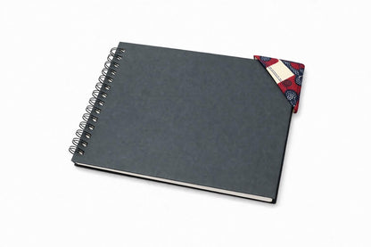 Black spiral-bound notebook with a cream, maroon, & blue corner bookmark on a light gray background