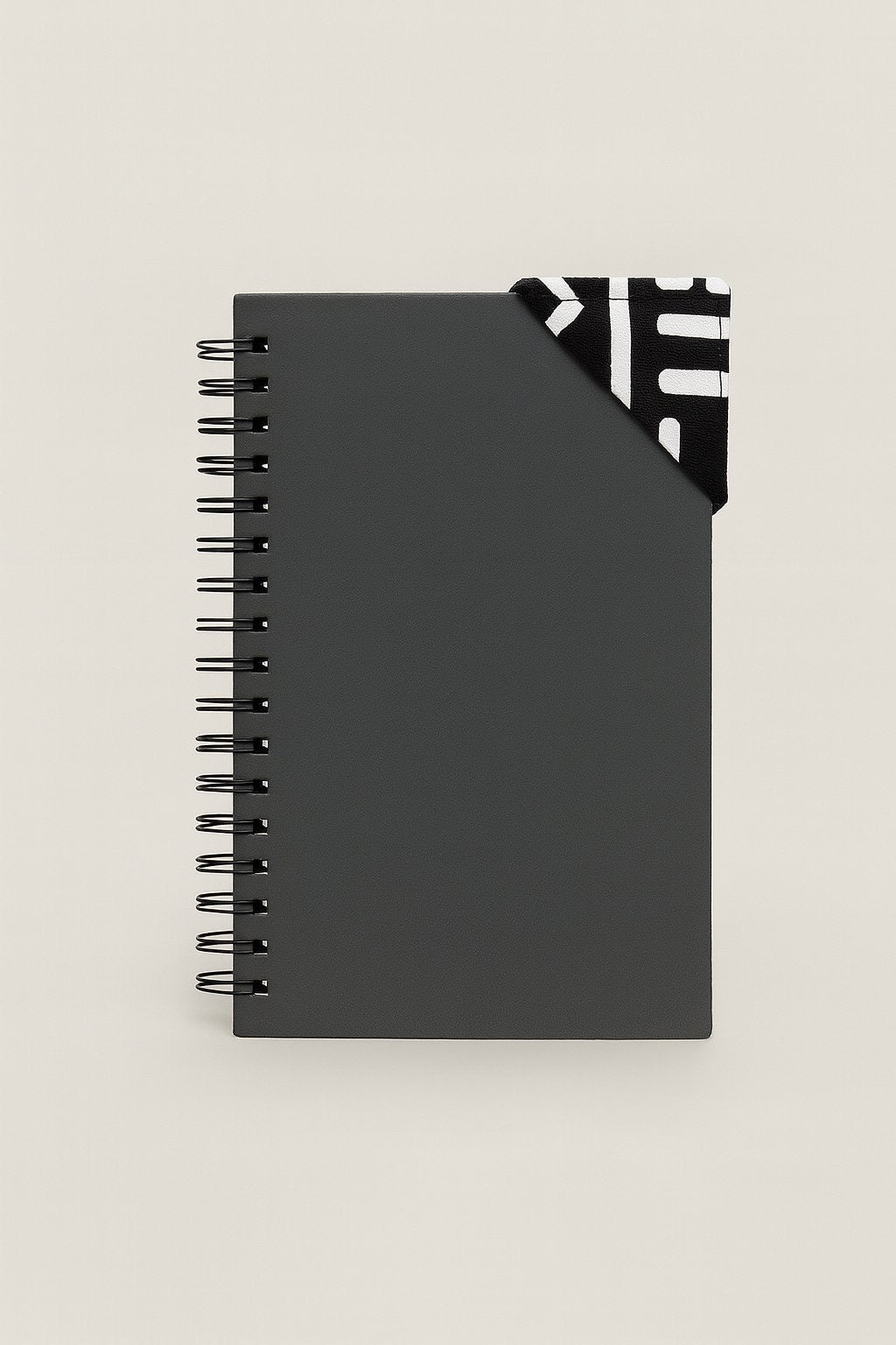 Black spiral-bound notebook with a black and white corner bookmark on a light gray background