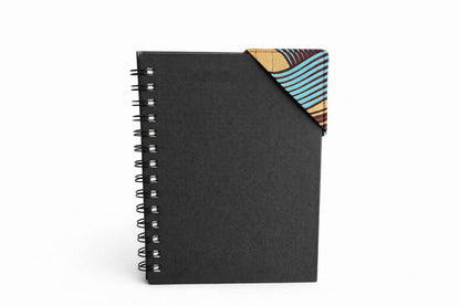 Black spiral-bound notebook with a brown, turquoise, & gold corner bookmark on a light gray background