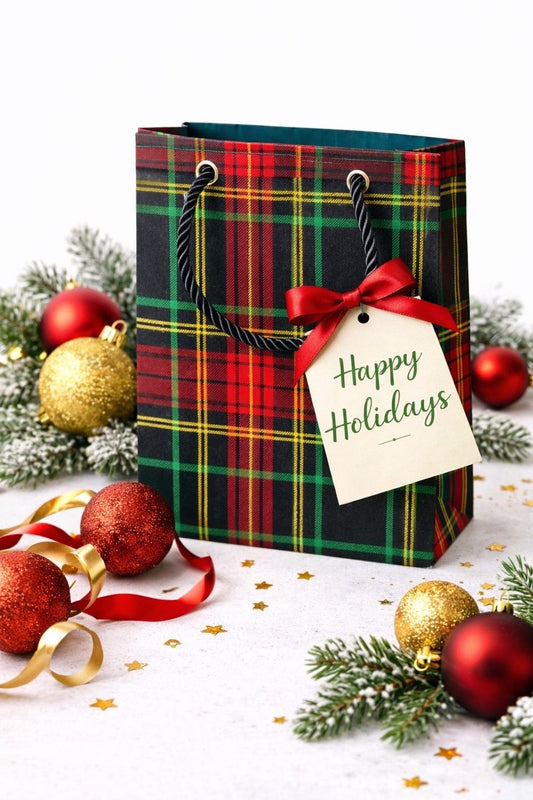 Black, red, green, & gold extra small gift bag on white background with ornaments, ribbons, gift tag, confetti, & tree branches