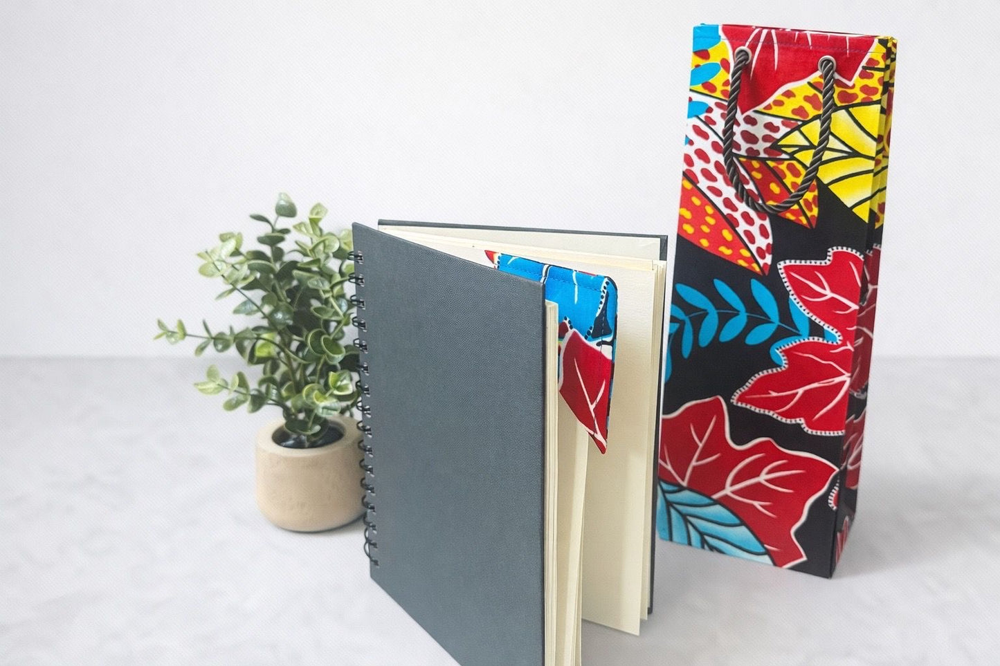 Black, white, yellow, blue, & red wine bag & corner bookmark on a black spiral notebook on a white background